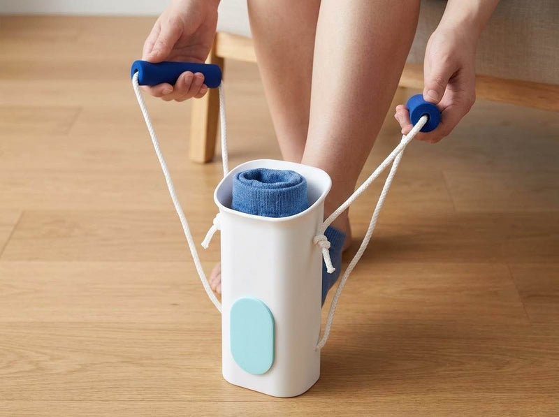 A loaded sock aid stands on a wooden floor while both blue foam handles are held, one in each hand.