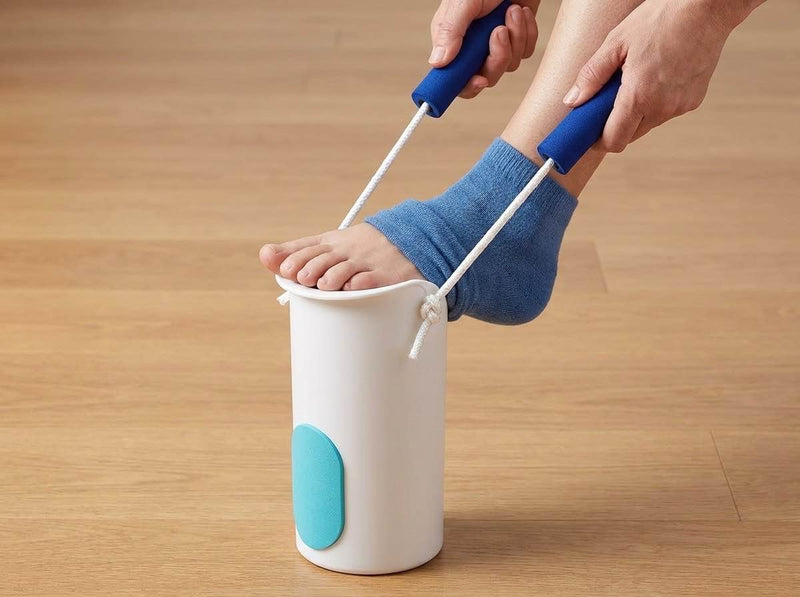A foot enters the cradle of a sock aid as both corded handles are pulled straight up and the blue sock rises.
