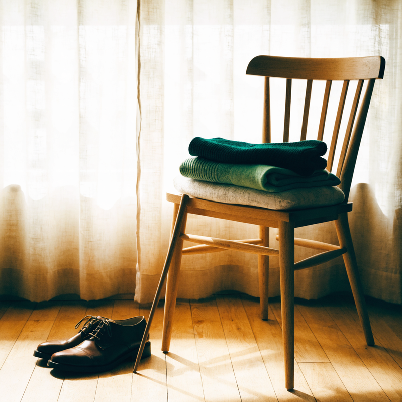 Shoes and a long handled shoehorn beside a bedroom chair with folded knitwear