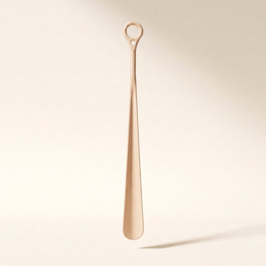 Long-handled shoehorn standing upright on a soft cream studio background, showing the full 23.6 inch reach and hanging ring