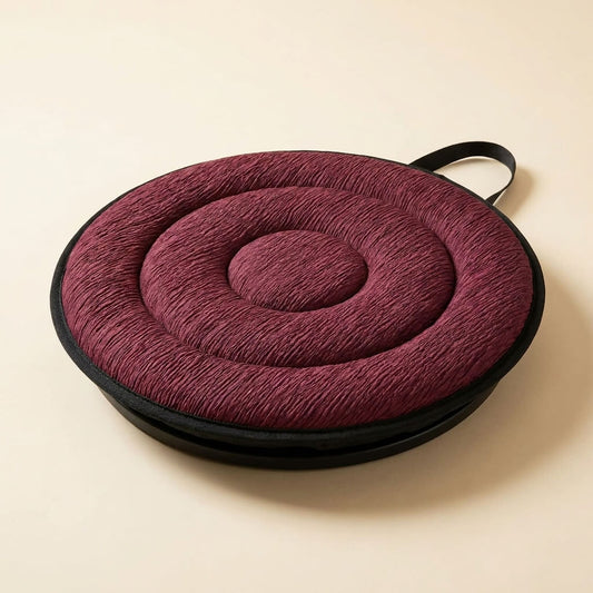 Burgundy 360-degree rotating seat cushion with carry strap on a warm cream studio background