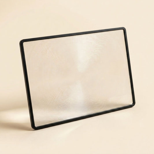Full-page fresnel magnifier propped on a cream studio background, showing the rigid frame and lightweight page-sized lens