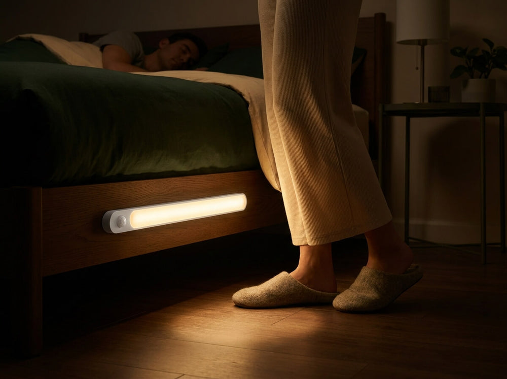A warm light bar on a bed frame lights the floor as someone in slippers steps out of bed at night.